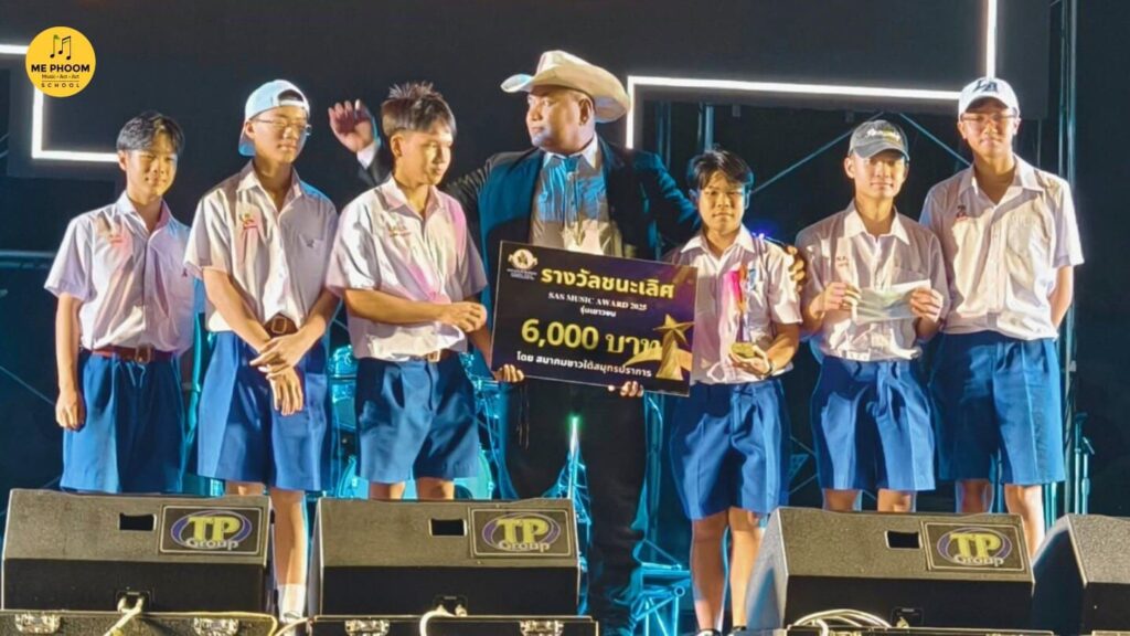 วงดนตรีนักเรียน PENMANSHIP 7 คนในชุดนักเรียนยืนอยู่บนเวทีพร้อมกับผู้ชายสวมหมวกคาวบอย โดยนักเรียนถือป้ายรางวัล 'SAS MUSIC AWARD 2025' และเงิน 6,000 บาท แสดงถึงชัยชนะการแข่งขันดนตรี