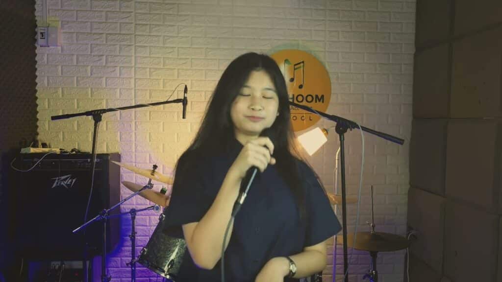 นักเรียนหญิงกำลังฝึกร้องเพลง Cover และอัดคลิปวิดีโอ ในห้องซ้อมดนตรี โรงเรียนดนตรีมีภูมิ (Me Phoom Music School) พร้อมบรรยากาศแสงไฟสตูดิโอ